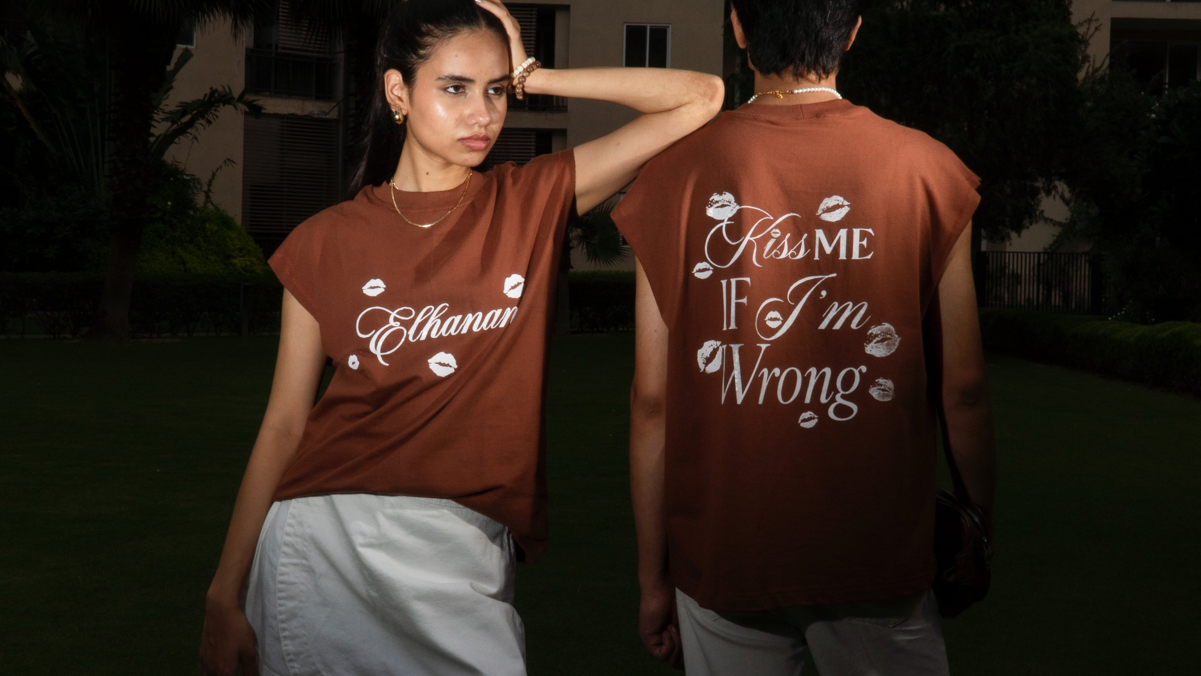 Two people wearing matching brown t-shirts with text, standing outdoors at night.